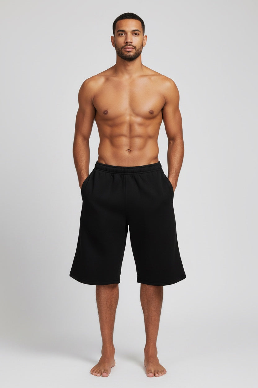 A shirtless man modeling black knee-length shorts against a light gray studio background.