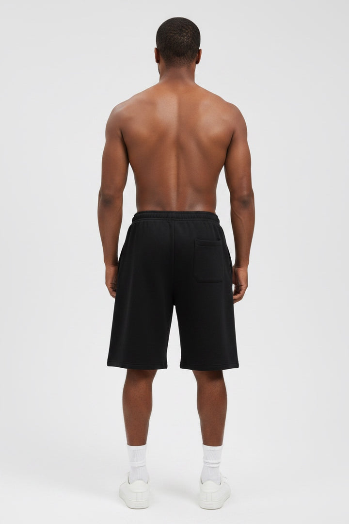 A man viewed from behind wearing black athletic shorts, white socks, and white sneakers against a light gray studio background.