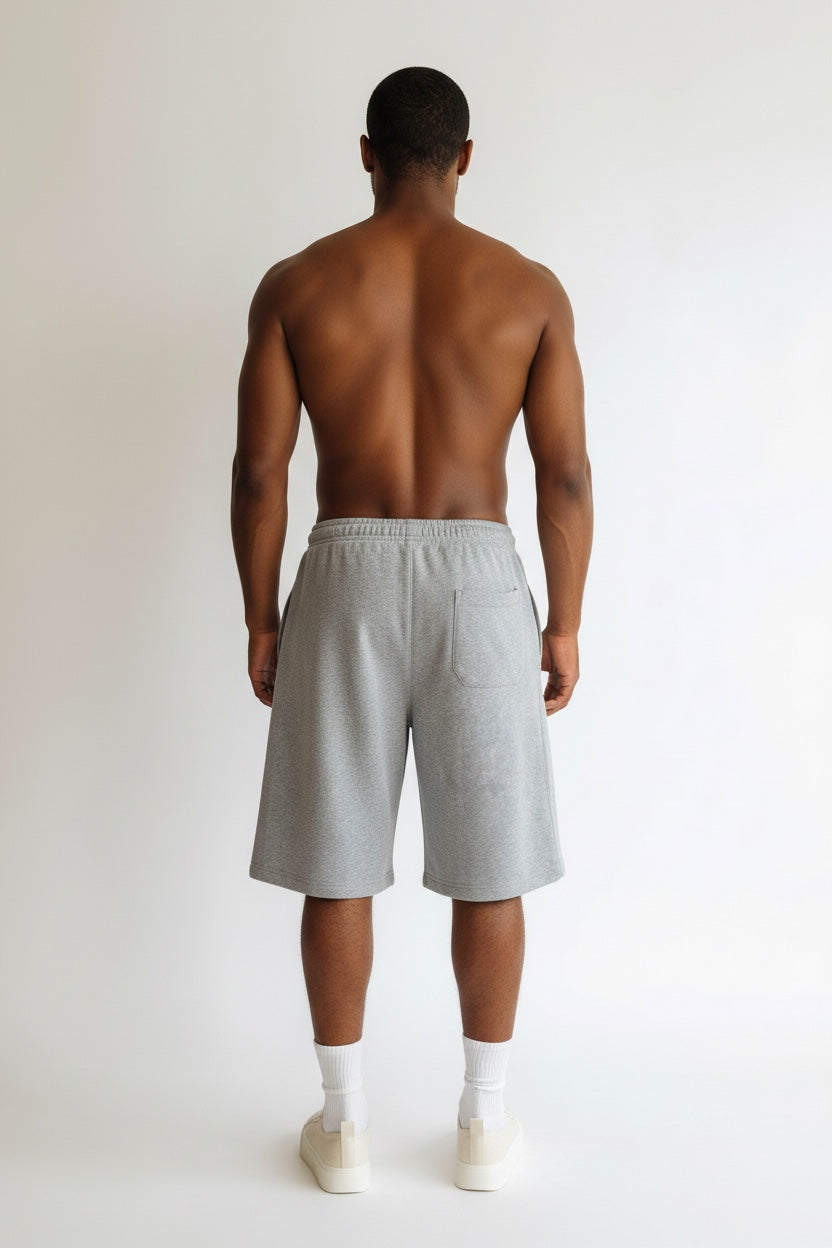 A man viewed from behind wearing light gray heather sweat shorts, white socks, and white sneakers against a plain white studio background.